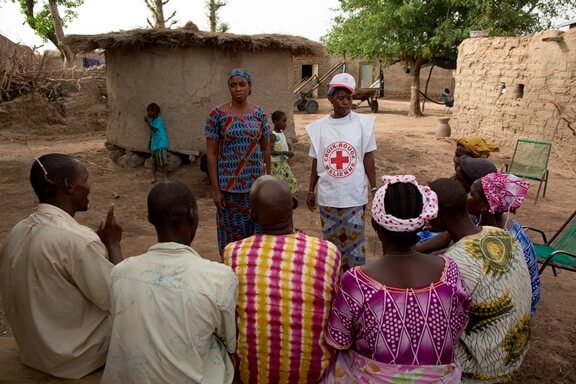 a small crowd listens to a Red Cross worker teach