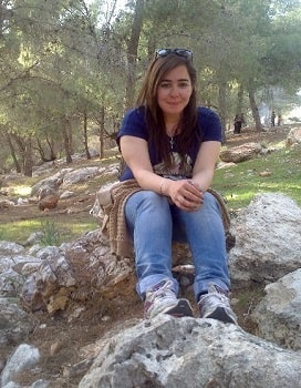 A young woman sitting on a large rock with trees in the background