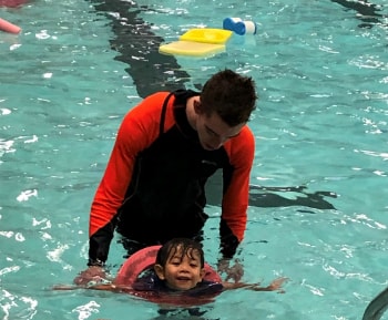 Kai swimming in the water with his swimming instructor