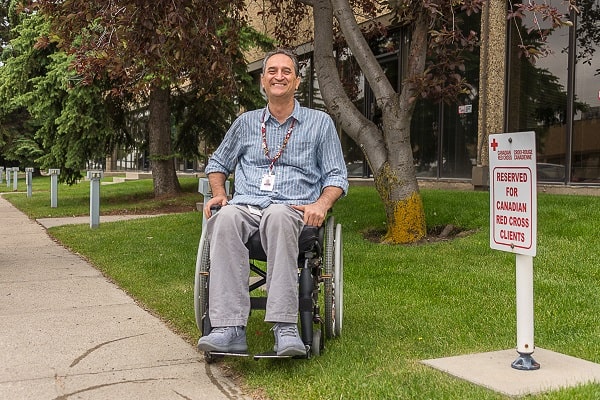 Canadian Red Crosser Mahmood Jafari smiling from his wheelchair outside a building.
