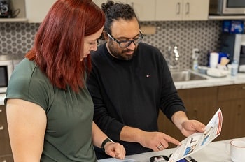 Man and woman reviewing instructions together in a kitchen. They are learning how to give naloxone.
