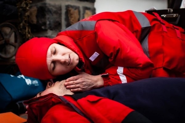 A Red Cross member leaning over a person checking for breath.