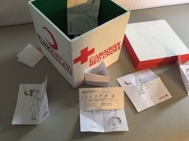 a box decorated with a Red Cross and a Red Crescent with the lid open and children's drawings showing