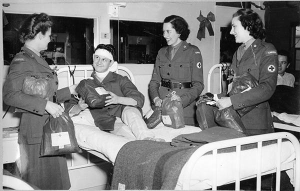 Three CRCC Welfare Officers visit a convalescing soldier overseas (ca. 1943-45) while distributing “ditty bags” on a hospital ward.