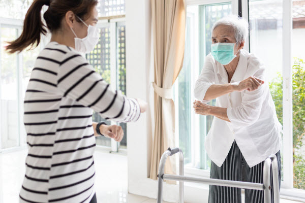 A young woman leads an at home exercise with an elderly woman, both wearing surgical masks.