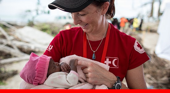 Red Cross volunteer holding baby girl.