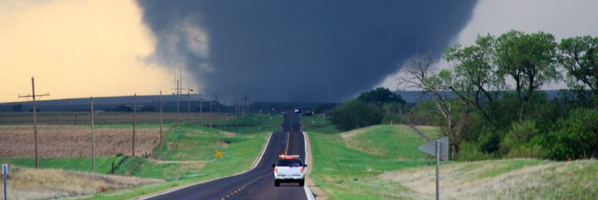 An emergency vehicle drives along a road towards a tornado