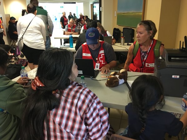 two volunteers in red vests sitting across from a family of evacuees at a table