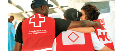 Three Canadian Red Cross volunteers wearing red vests wrap their arms around each other in an open hug.