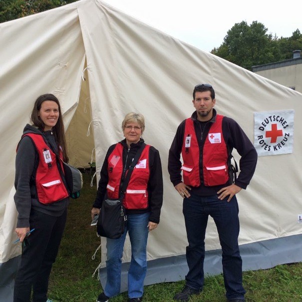 Three people wearing Red Cross vests standing outside a white tent