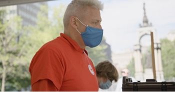 a person in a red polo shirt and blue face mask, delivering supplies in a park