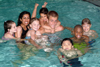 Two adults and seven kids playing in a pool