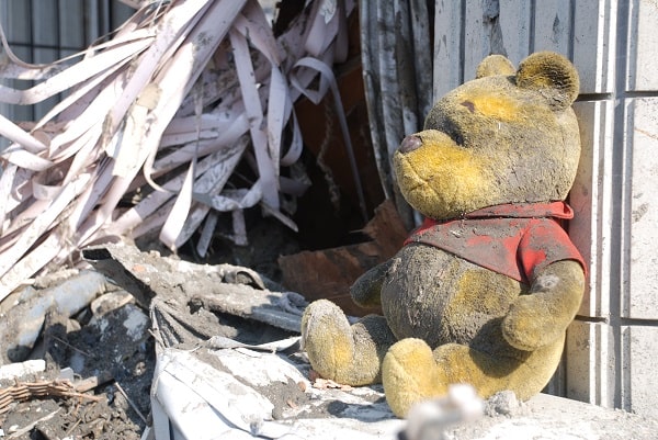 A Winnie-the-Pooh toy covered in dirt sits against a wall.