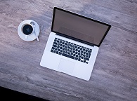 A laptop on a table with a cup of coffee beside it.