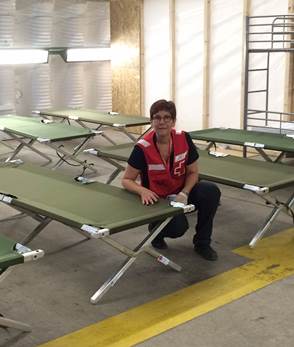 A woman in a Red Cross vest sitting by an empty cot in a room full of empty cots
