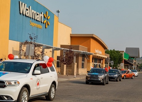 Cars decorated in red and white balloons in a single file parade outside a Walmart store.