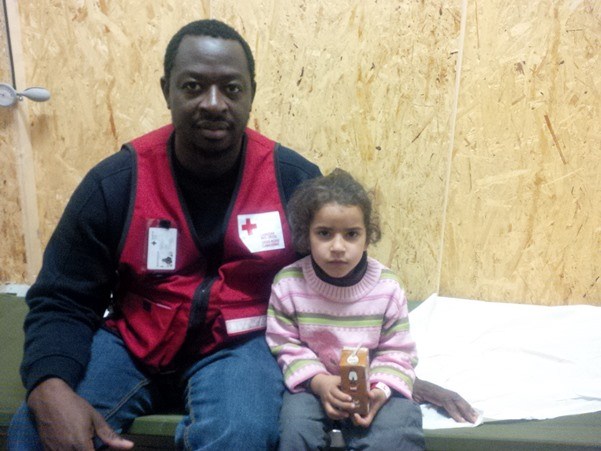 A man in a Red Cross vest sitting beside a young girl