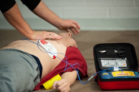 A pair of arms shown with hand on chest and AED hooked up to mannequin
