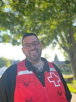 A man in Red Cross vest smiling from under a tree