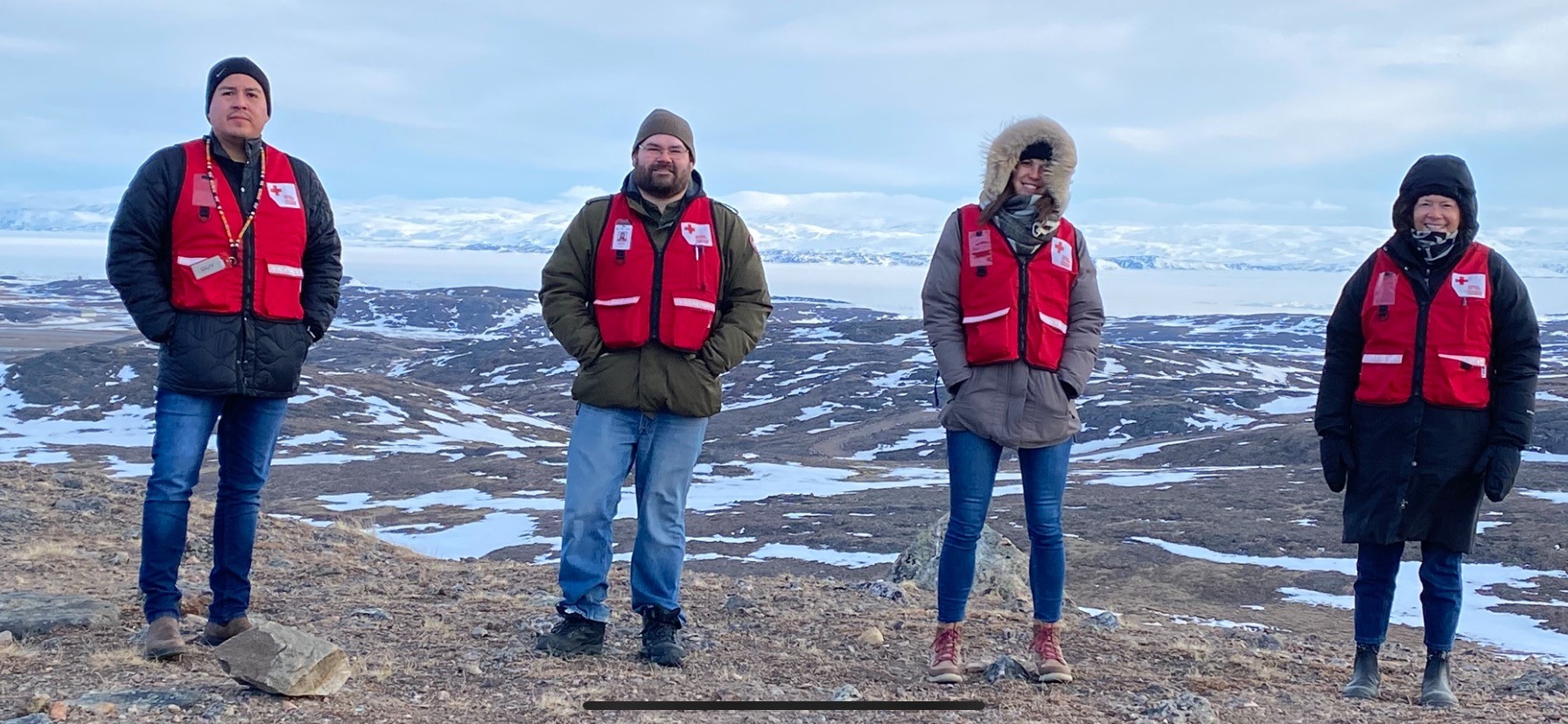 Red Cross team in red vests and winter coats standing on a snowy landscape in Iqaluit.