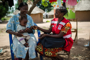 A South Sudan Red Cross personnel talks to a smiling woman holding a baby.