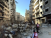 Two Red Cross workers in the ruin of a city, surrounded by debris. 