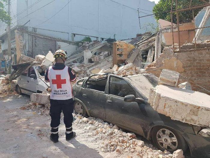 A Red Cross worker looks on at a collapsed building