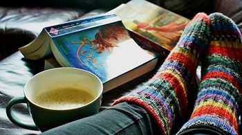 A closeup of warm cozy socks, a cup of coffee, and two novels on a couch.