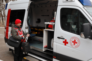 A member of the Ukrainian Red Cross Society carries health equipment, standing outside of a Mobile Health Unit.