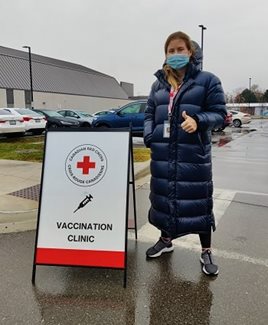 A woman in a mask standing outside beside a sign that reads Vaccination Clinic