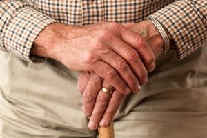 A seniors' hands resting on top of a cane.