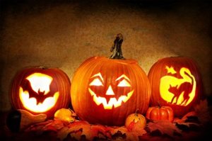 Three jack-o-lanterns sitting beside uncarved pumpkins