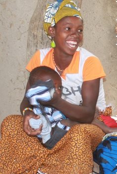 A Smiling woman sitting with a small child in her arms.