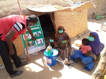 Mali Red Cross volunteers conducting outreach activities with a group of women and children sitting by a house