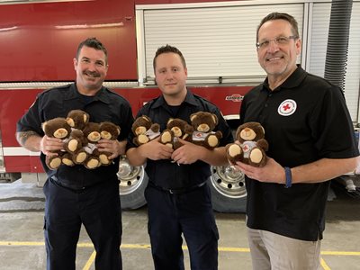 Red Cross volunteer and firefighters hold teddy bears
