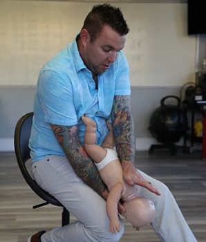 A man holding a mannequin baby in a CPR technique on his forearm