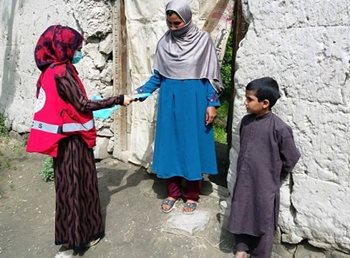 A member of the Afghan Red Crescent handing material to a woman with a young child.