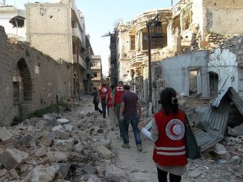 Red Crescent members walking through a destroyed street in Syria.