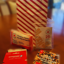 A gift bag, gift cards, and Canadian Red Cross emergency tissues and bandages assorted on a table.