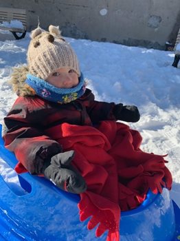 A small child sitting on a sled in full winter wear