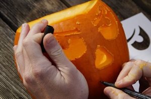Hands carving a face into a pumpkin
