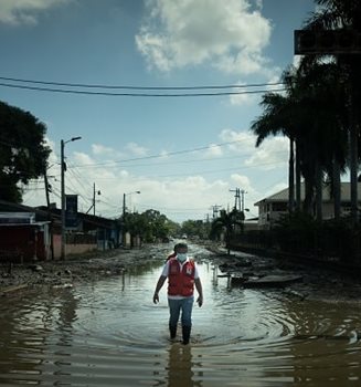 A Red Cross member walking down a flooded street