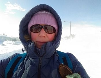 A woman in winter gear and sunglasses on a snowy street.