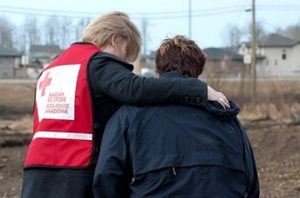A Red Cross volunteer wearing a red vest provides a comforting hug to another person