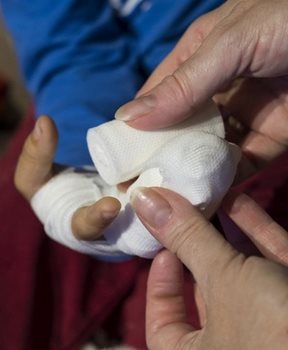 An adult hand wrapping a child's hand in a bandage.