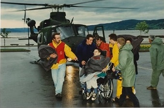 Red Cross helps evacuate a group of people, one in a  wheelchair, from a helicopter