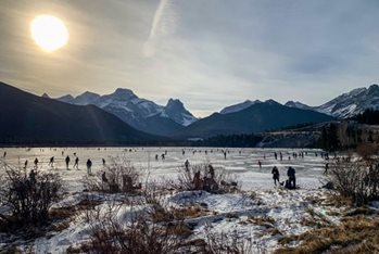 Sun shining on frozen lake with people skating on it