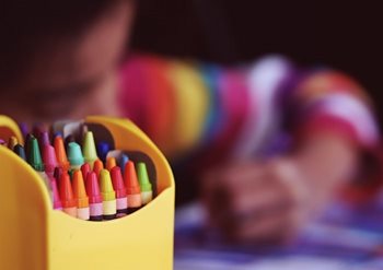 A child using crayons from a colourful box in the foreground. Photo: Aaron Burden