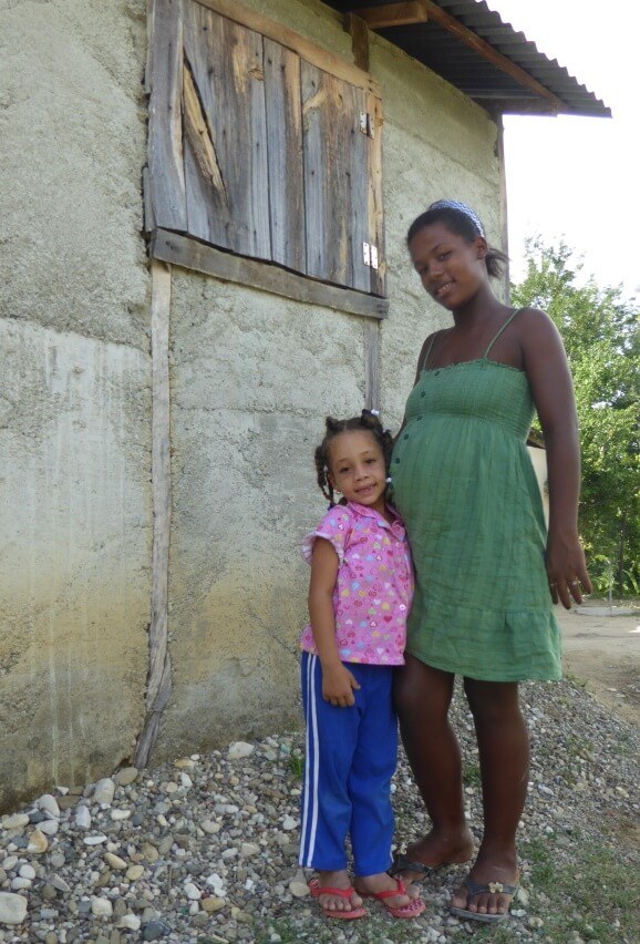 pregnant woman stands with little girl beside house