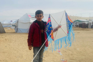 Amr’s son Adam stands outside with a colourful kite. Several white tents are visible behind him.